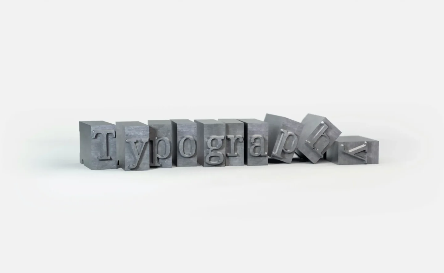 Alt Description: Metal letterpress blocks spelling Typography with some letters toppled over on white background.