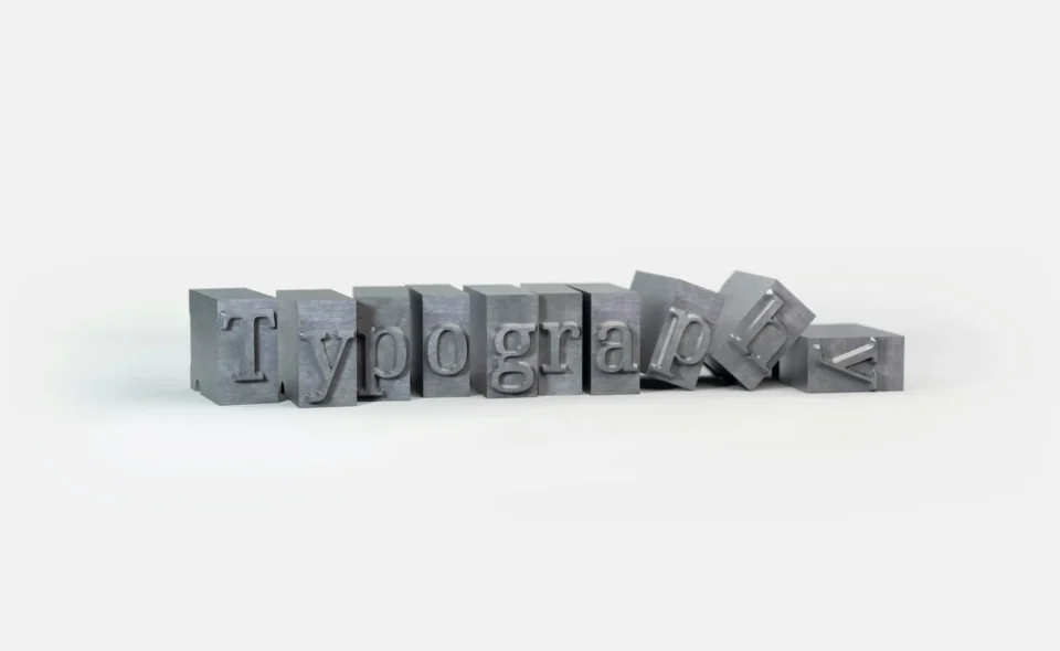 Alt Description: Metal letterpress blocks spelling Typography with some letters toppled over on white background.