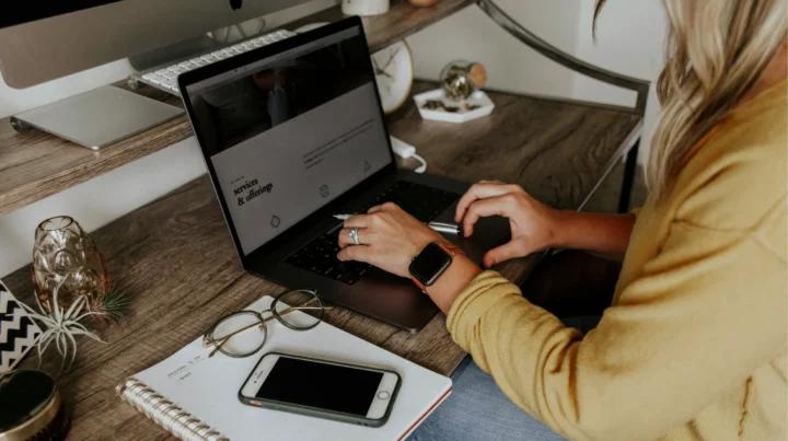 Web designer reviewing a services and offerings page on a laptop while working at a wooden desk, representing the small business website design process.