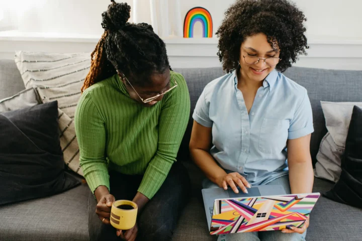 Two women sitting on a couch reviewing a laptop together while consulting on a small business website design project.