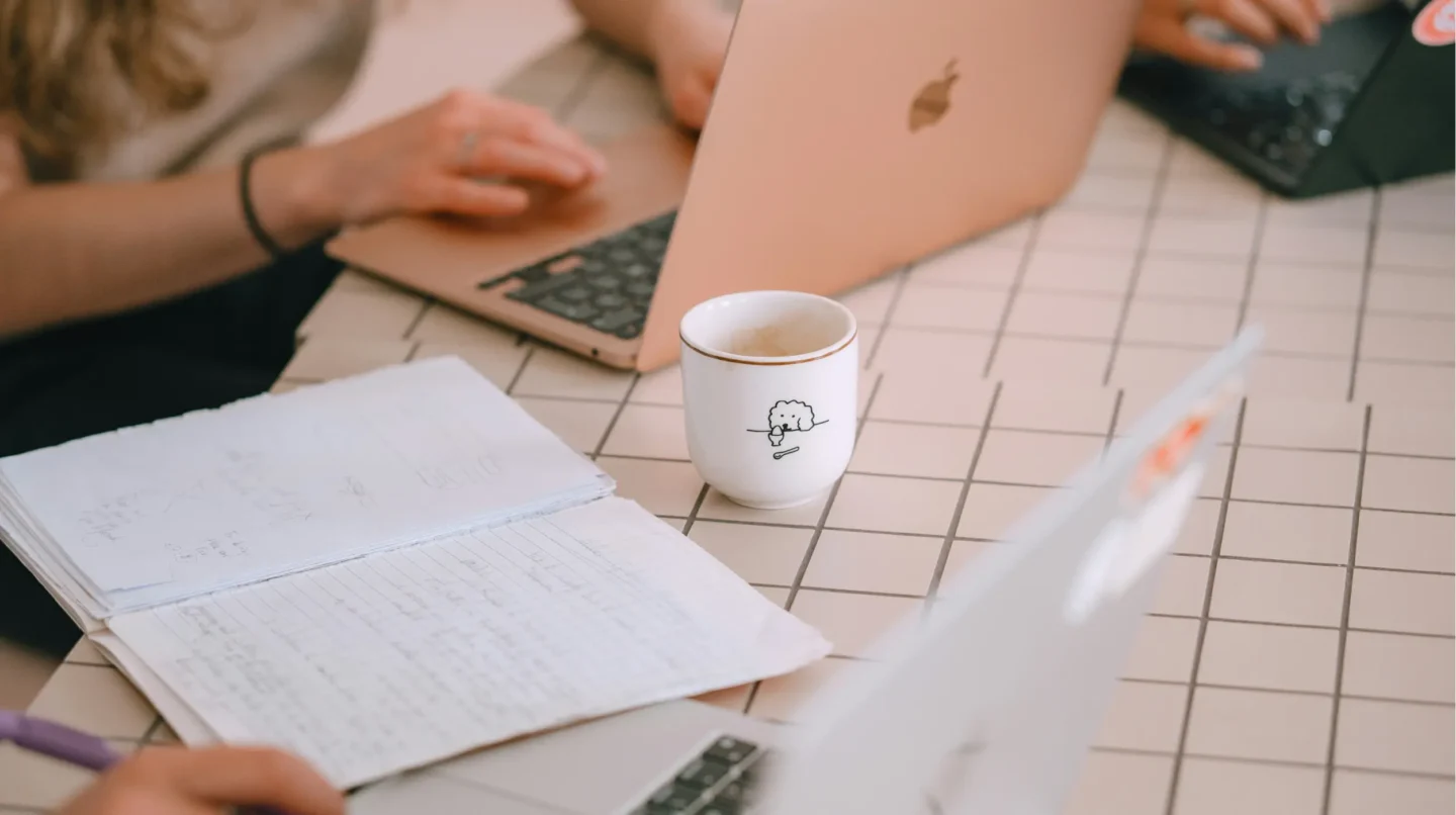 Two people working on laptops with handwritten notes and a coffee cup on a grid table, planning a website project