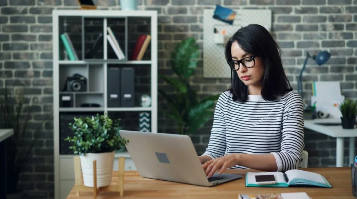 A small business owner with glasses works on a laptop at a modern home office desk, evaluating her small business website for signs it needs a redesign.